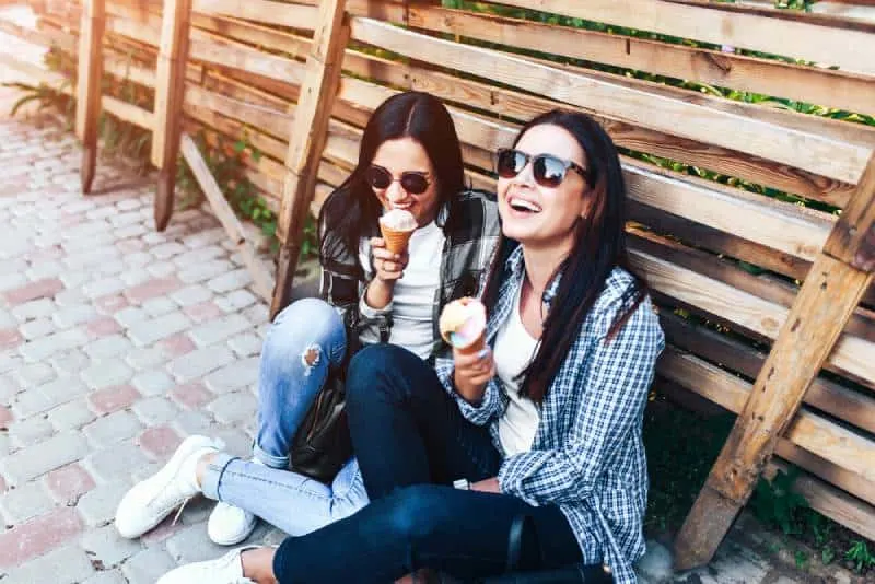 two smiling brunette girls eating ice cream outdoor