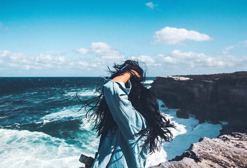 woman holds hair and stands in front of sea