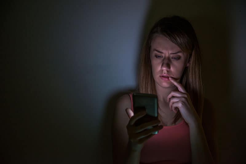 mujer preocupada mirando su teléfono durante la noche en su casa
