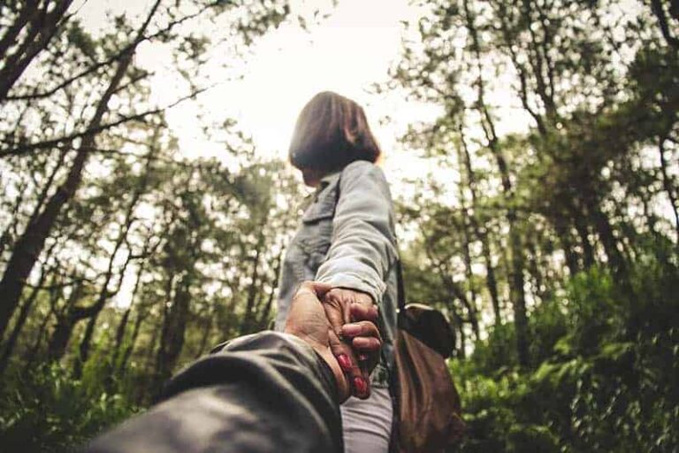 woman holds man's hand beside trees
