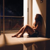 uma rapariga triste e deprimida sentada no chão junto à janela