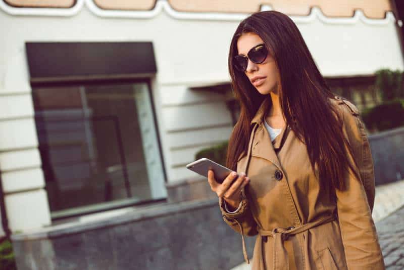 Beautiful young woman in trench using her mobile phone