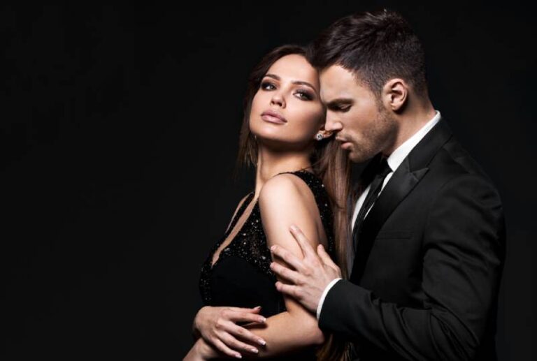 man in suits hugs from back woman in black dress with black background