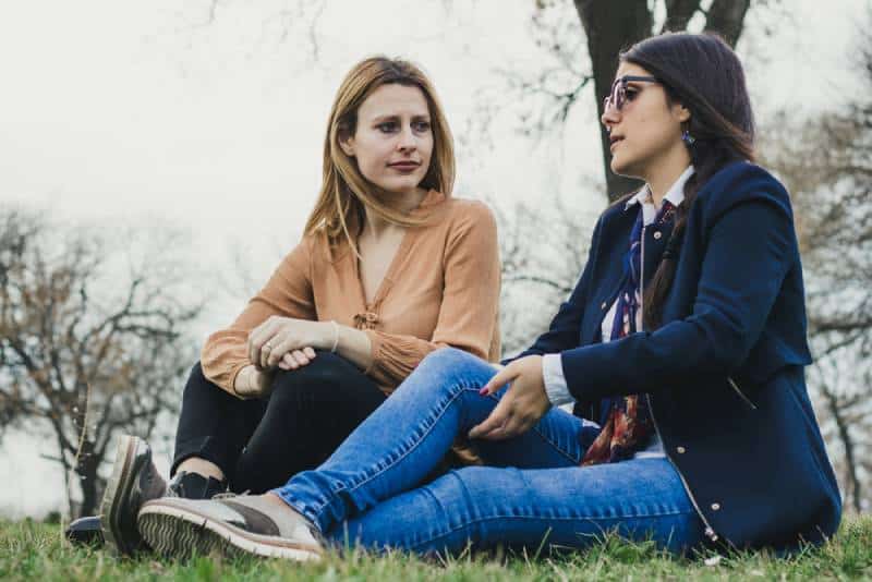 Due giovani ragazze silvane sedute sull'erba a raccontarsi tristi storie di vita, in un parco in una bella giornata di primavera.