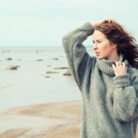 mujer con un cálido cárdigan en la fría playa