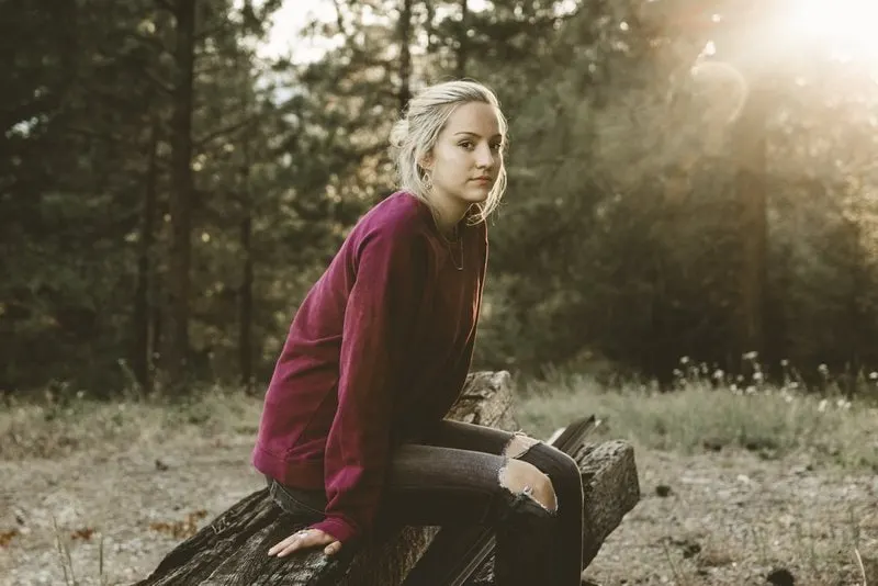 a blonde in a burgundy sweater sits on a park bench
