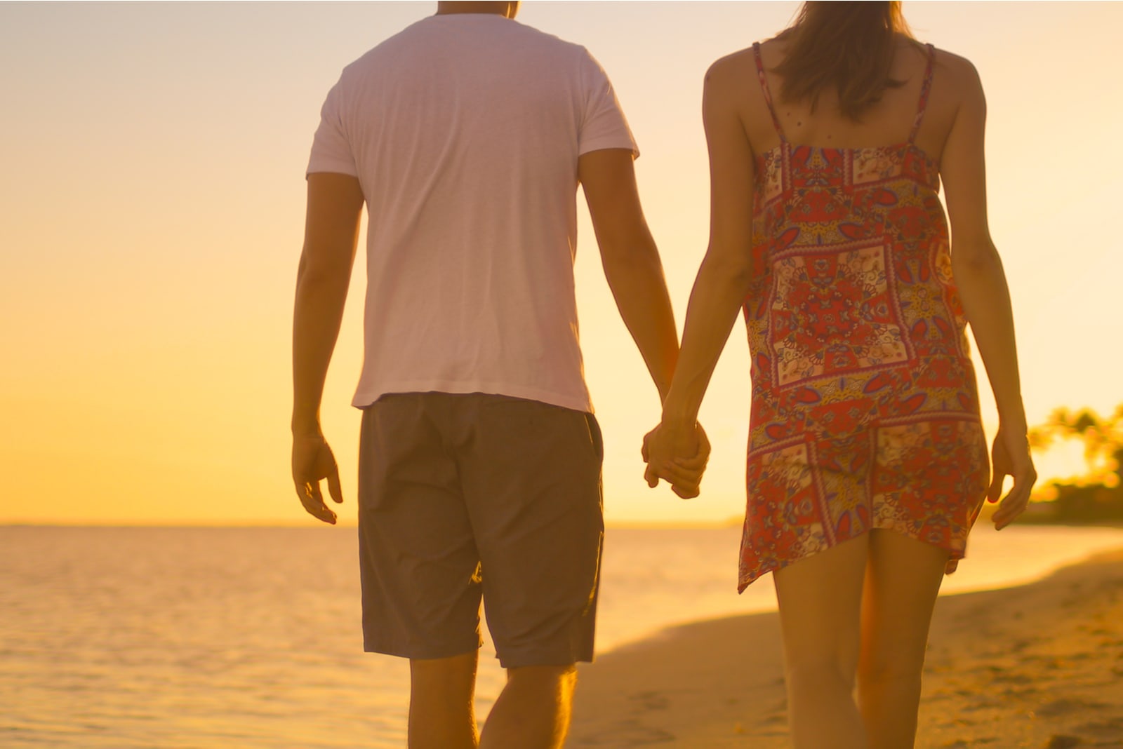 un uomo e una donna camminano lungo la spiaggia tenendosi per mano