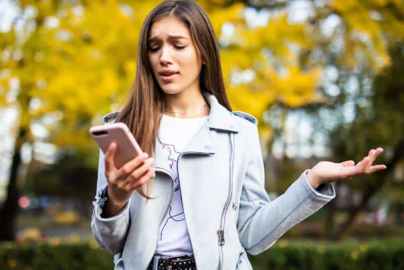 confused lady looking at her phone in city park