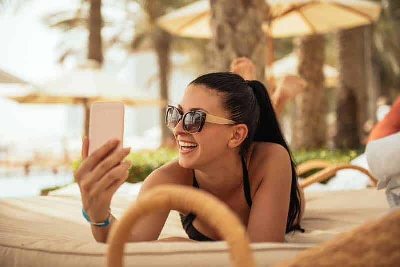 mulher feliz com óculos de sol e a olhar para o telemóvel