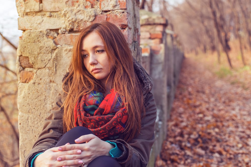 outside in the fall sits a sad woman leaning against a wall