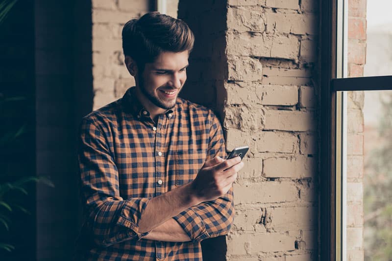 uomo sorridente che scrive al telefono