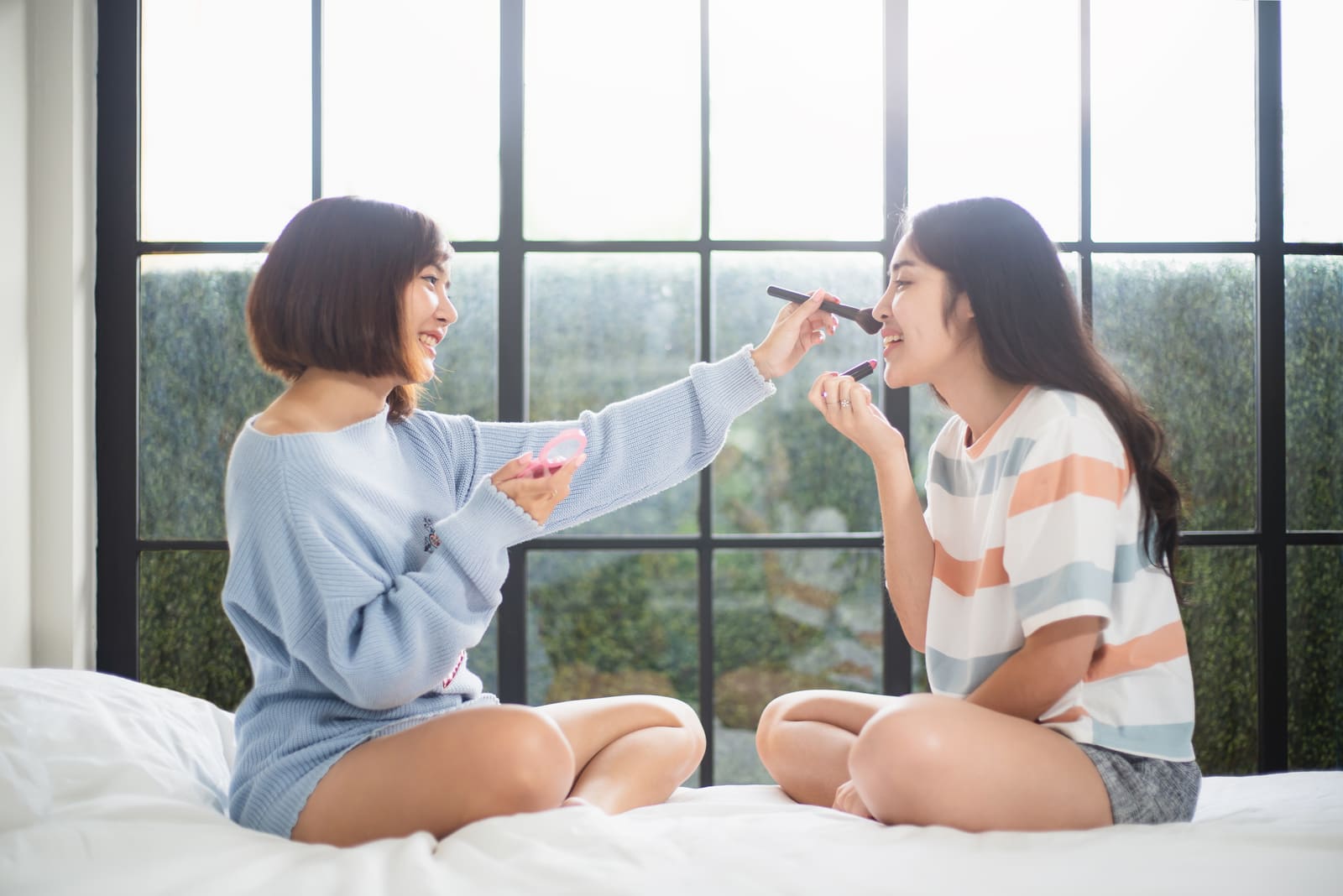 two friends sit on the bed and put on makeup