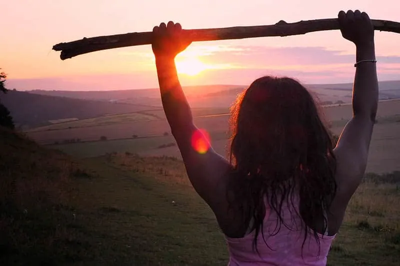 woman holds wooden branch up and looking at sunset