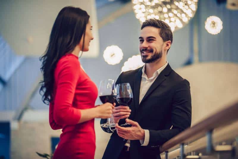 donna in abito rosso e uomo affascinante in giacca e cravatta che conversano con un bicchiere di vino