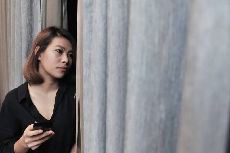 worried woman holding phone and looking outside