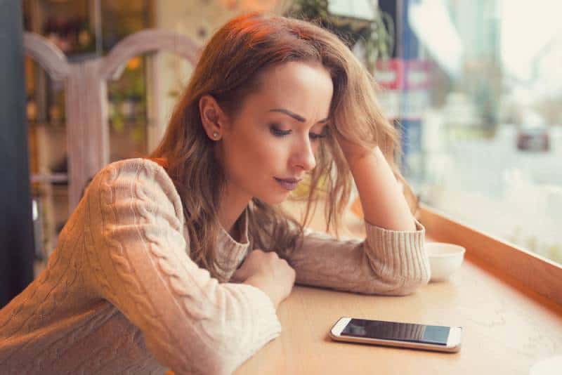 mujer preocupada mirando el teléfono en una cafetería