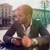 man in suit holding phone and sitting in street cafe