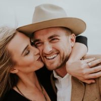 woman kisses smiling man with hat
