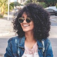 mulher afro com óculos de sol e a sorrir no exterior