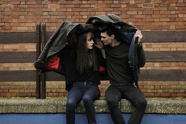 man and woman sitting outside under covered with jacket