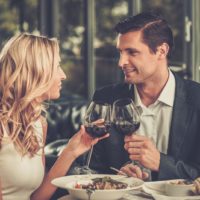 Pareja alegre en un restaurante con copas de vino tinto