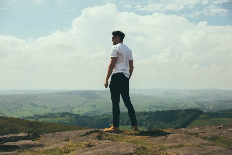 Uomo in piedi su massi con vista sulle colline e sulle montagne