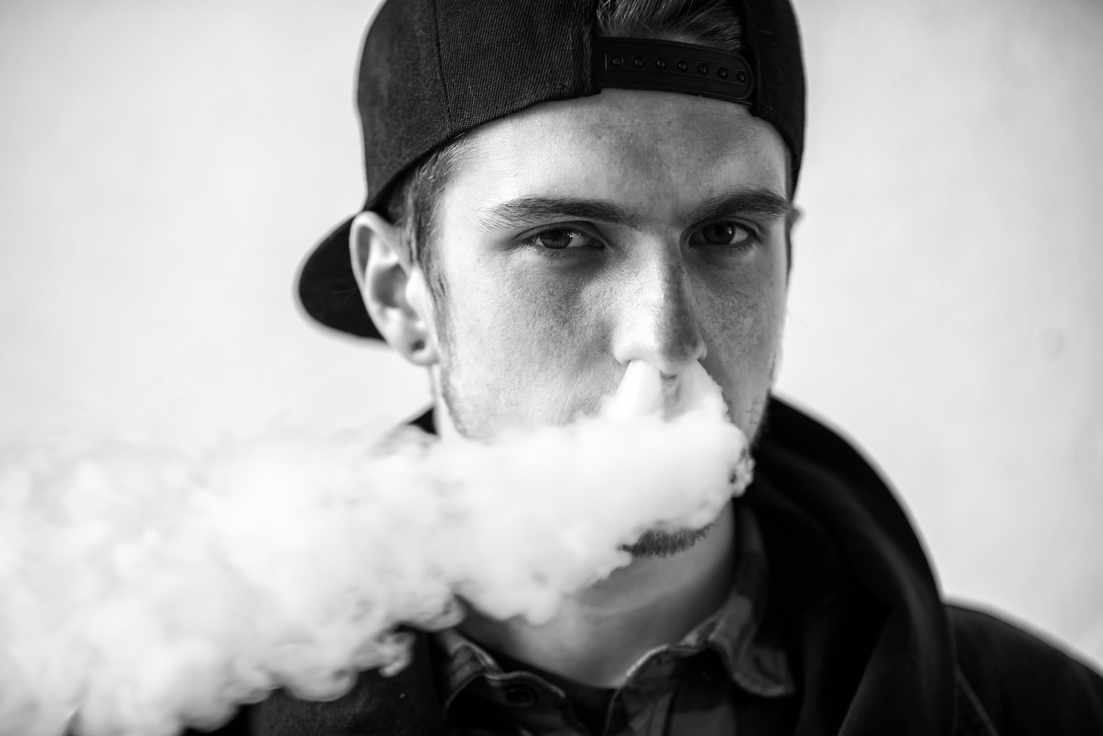 Retrato de joven guapo con gorra fumando un cigarrillo electrónico