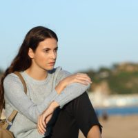 mujer mirando hacia otro lado sentada en la playa de una ciudad costera
