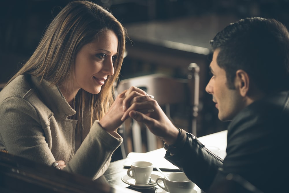 a man and a woman in love in a cafe sitting and holding hands