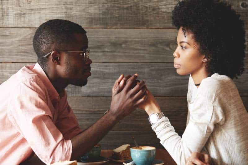 hombre negro con gafas cogiendo las manos de su bella esposa y pidiéndole perdón