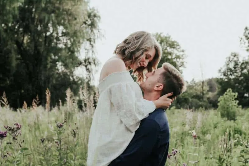 couple kissing each other around grass field