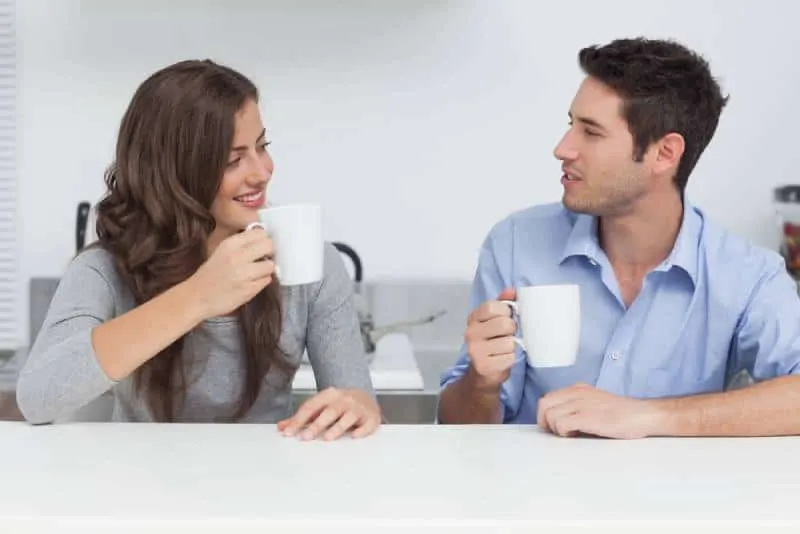 male and female talking and holding white cup of tea at home