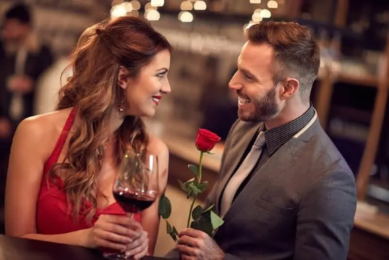 man holding roses standing in front of woman holding glass and looking each other