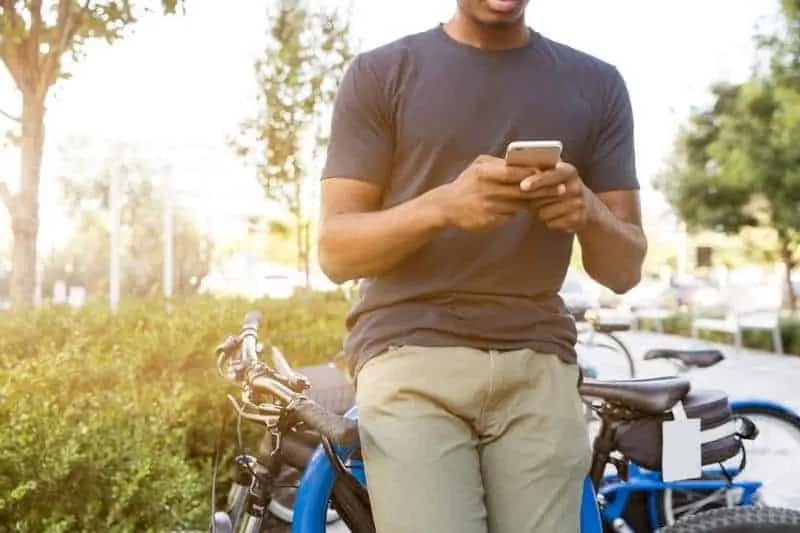 man typing on his phone while leaning on bike