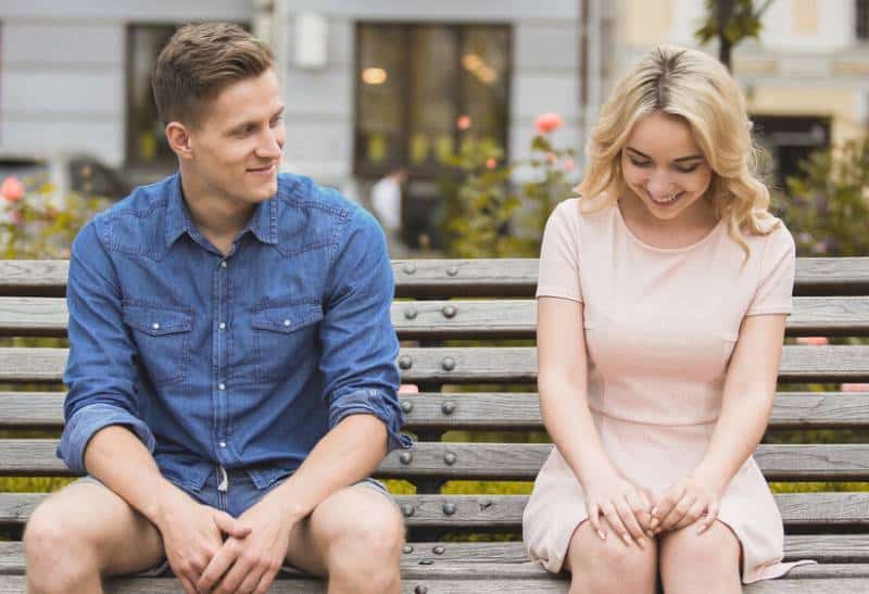 shy blonde girl sitting next to guy in blue shirt on a park bench