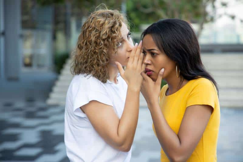 white women gossiping and whispering to black woman outside