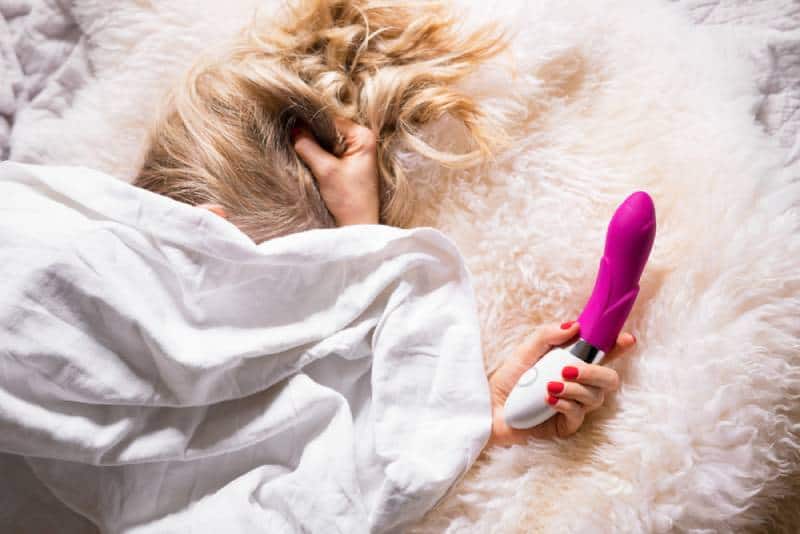 woman in bed under sheets holding vibrator