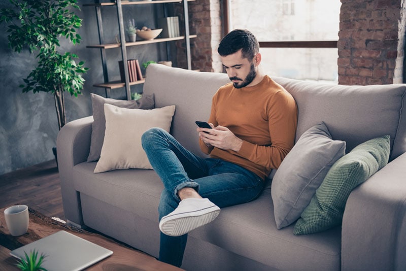 um jovem sentado no sofá e a enviar mensagens de texto