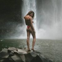woman in bikini standing beside waterfall