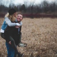 hombre feliz llevando a caballito a mujer sonriente en el campo