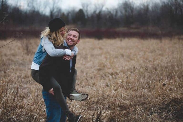 happy man piggybacking smiling woman on field