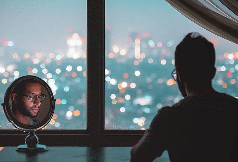 man sitting beside mirror and typing on phone