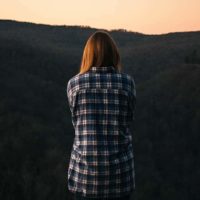 vista traseira de uma mulher de pé em frente de colinas