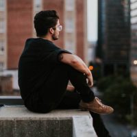 side view man in black shirt sitting on rooftop and looking at city