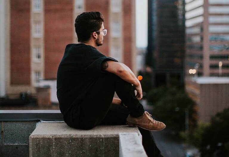 side view man in black shirt sitting on rooftop and looking at city