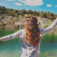 woman raising hand in front of water in nature