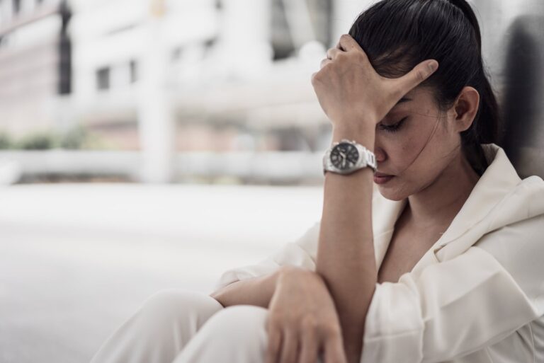 a disappointed woman sits outside and holds her head