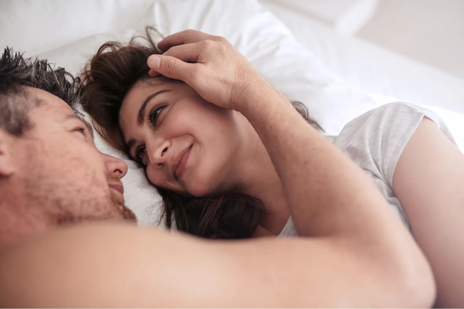 a man in bed caresses the face of a smiling woman