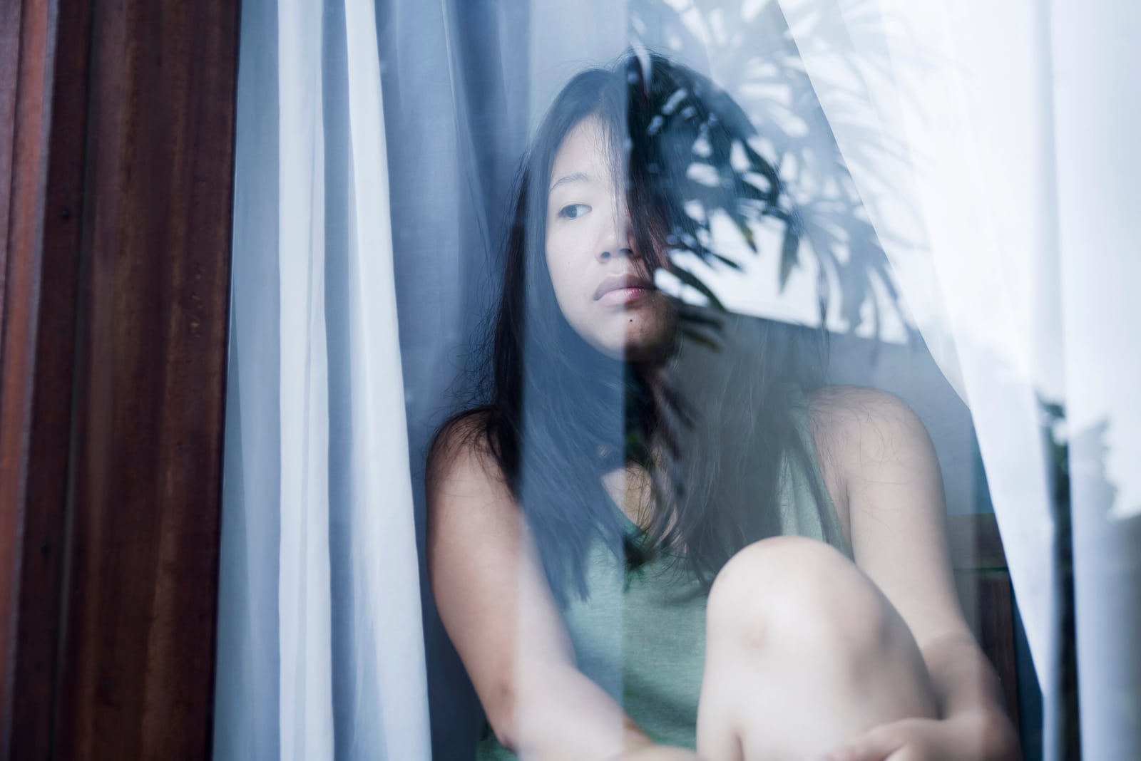 a sad Asian woman sits by the window and looks outside