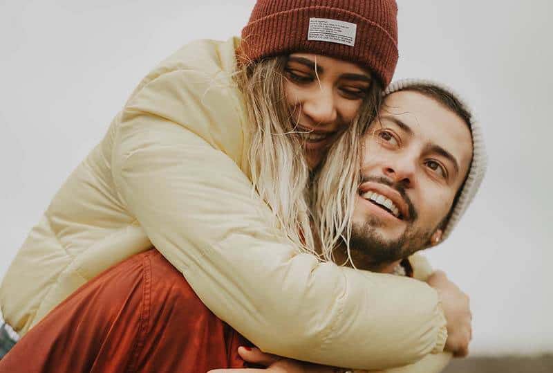 closeup man piggybacking smiling woman with hat